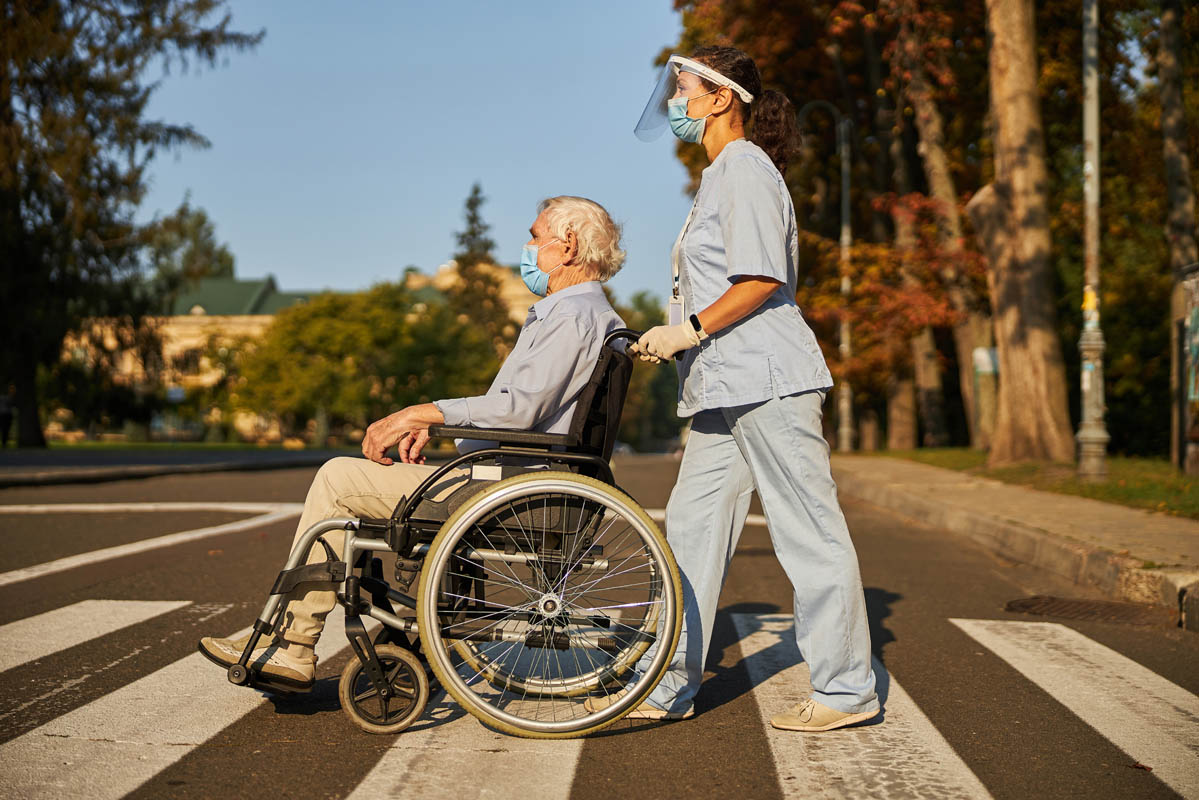 Smiling nurse helping senior man to walk around the city street